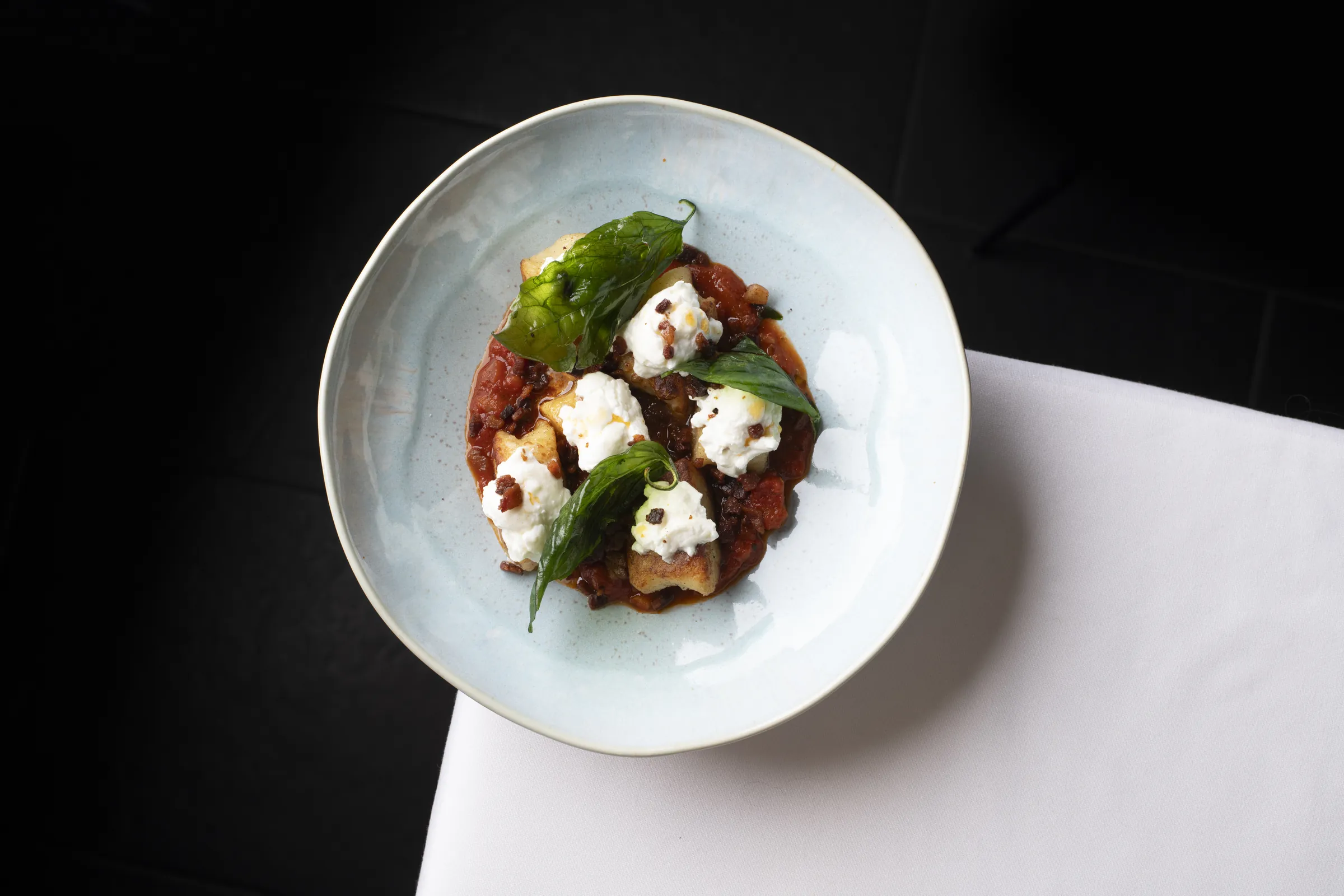 Burrata and basil over slow-cooked tomato, on a pale green plate at Saskia's
