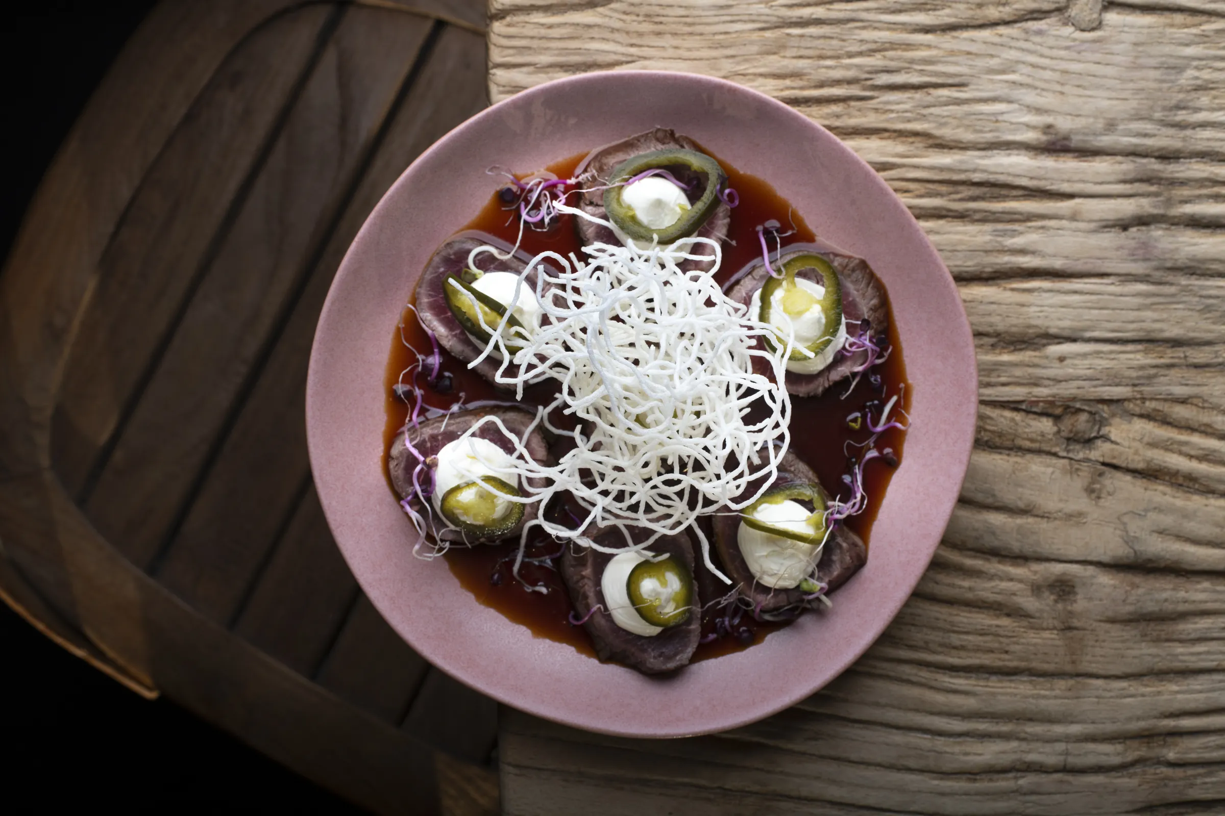 Beef carpaccio with pickled jalapeño and crisp noodle on a rose plate at Saskia's
